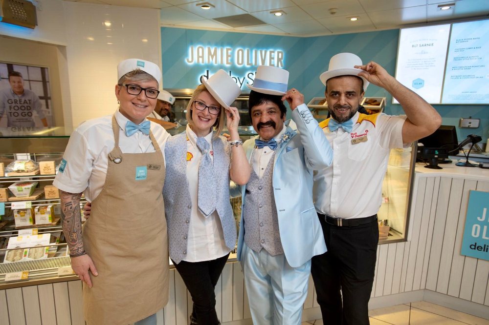 Nicola with four team members inside a Jamie Oliver Deli, all smiling and dressed in branded uniforms, celebrating a team milestone or launch.