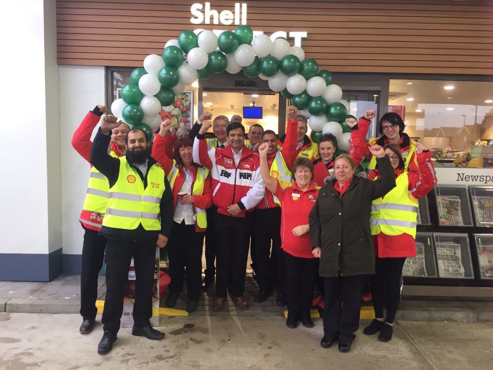 Nicola and a large Shell team gathered outside a Shell Select store, cheering and celebrating under a green and white balloon arch.
